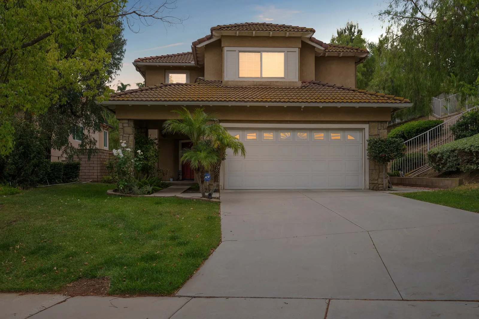 Two-story tile-roofed home at dusk with warm light in the windows