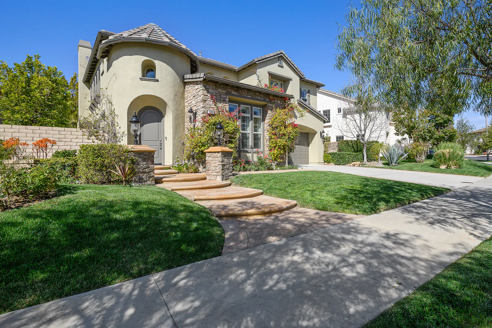 Two-story stucco home with a round tower, a stone-trimmed entry and curved steps across a green lawn