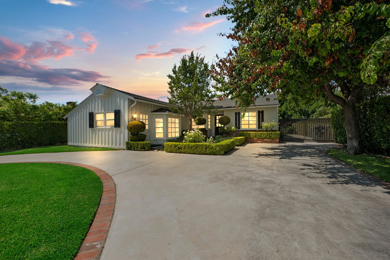 White single-story farmhouse-style home lit at dusk, with a circular driveway