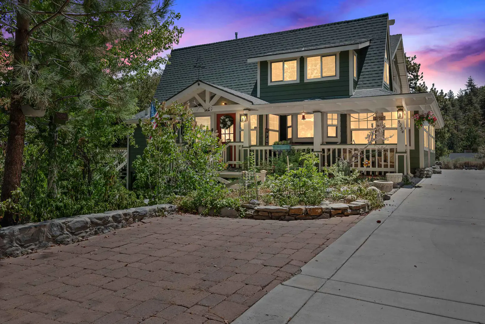 Green craftsman-style home with a wide front porch, lit at dusk