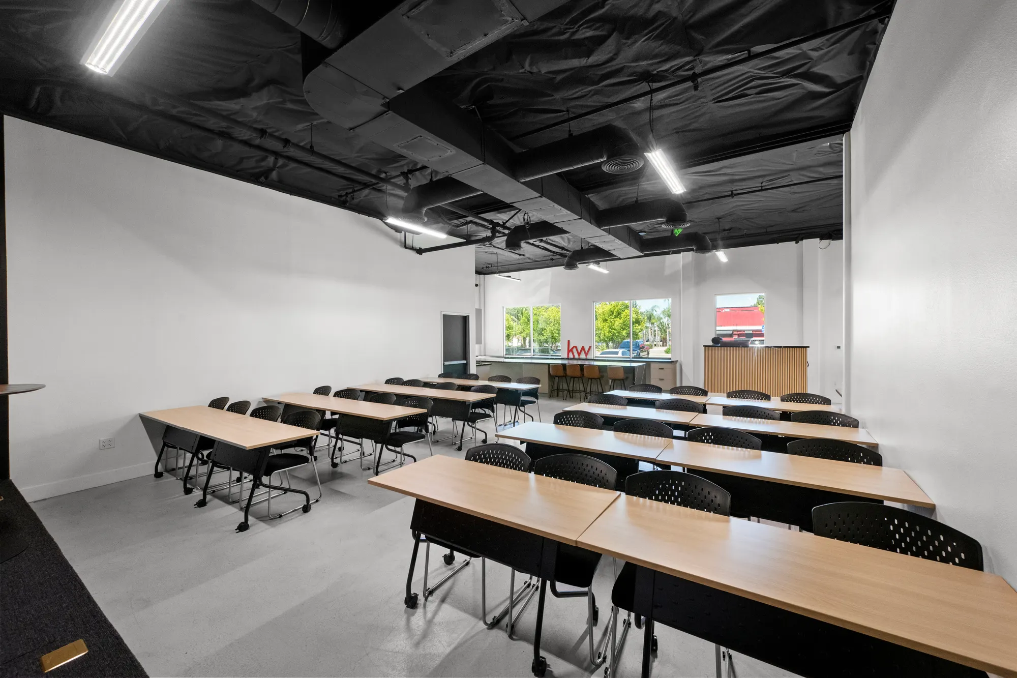 La sala de capacitación de la oficina: filas de escritorios de madera clara y sillas negras bajo un techo negro expuesto