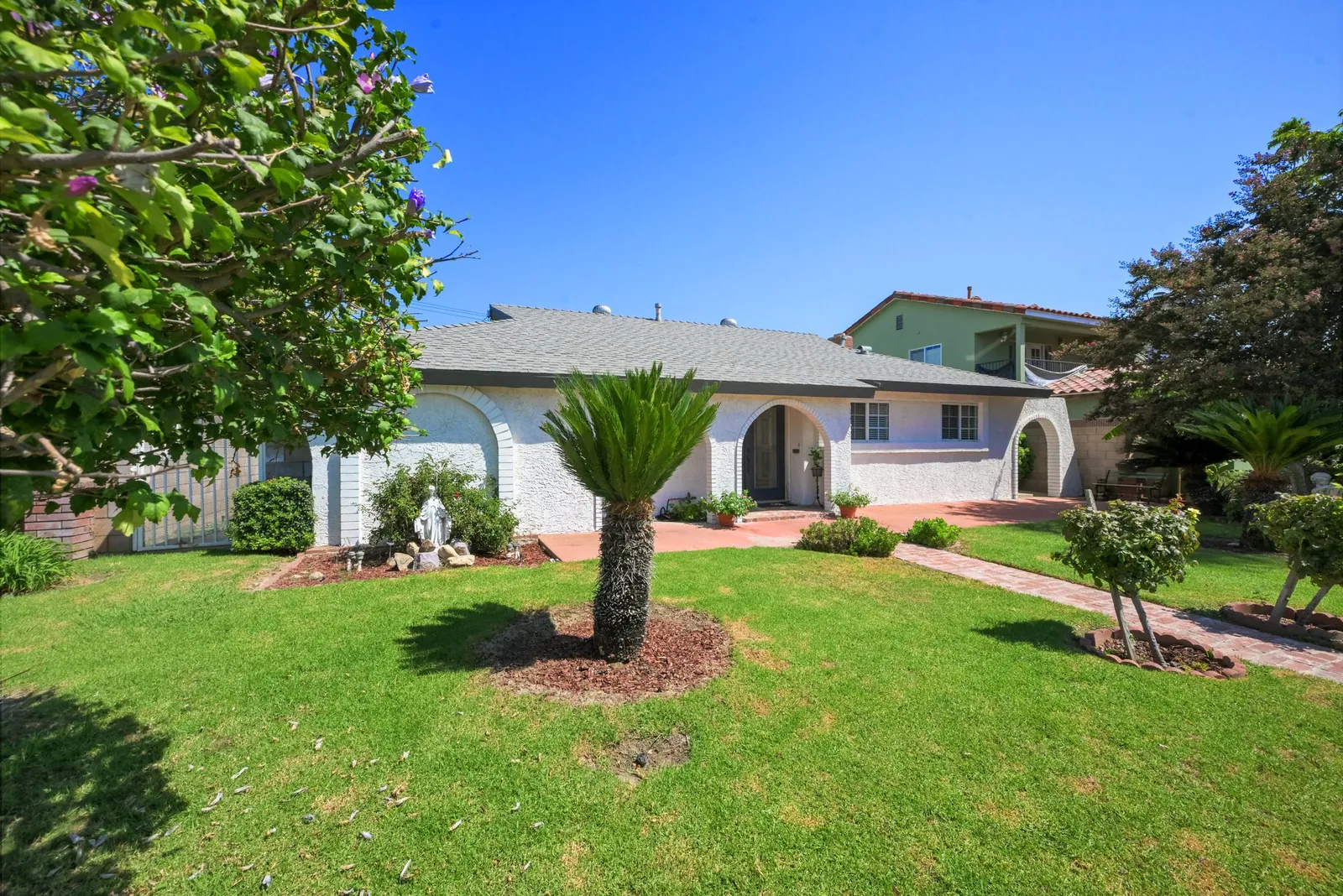 Single-story stucco home with arched entries and a sago palm on a wide front lawn